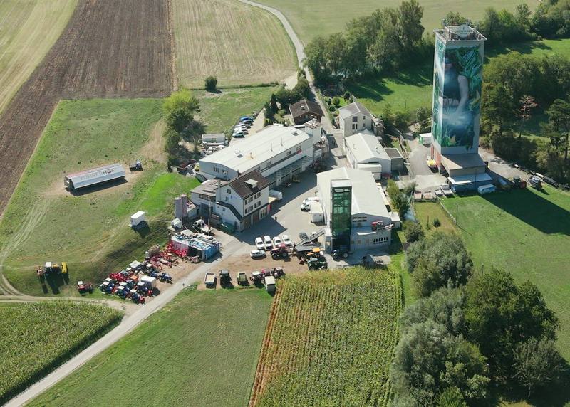 Luftaufnahme der Rheinmühle in Chur: Werkstatt, Maschinenplatz mit Traktoren und der bemalte Mühleturm